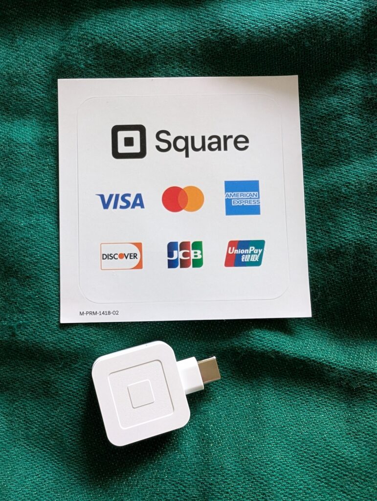 Photo of a small Square brand white mag card reader and a sticker with credit card logos on it on a green cloth
