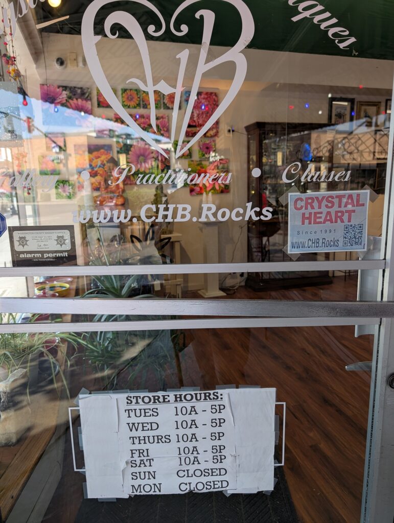 PHoto of a glass store front door with website CHB.rocks and other signage including the hours: Tues-Sat 10-5, closed Sun and Mon. The interior and some art and the wooden floor are visible through the glass.