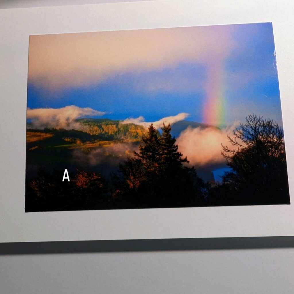 Photo showing a color photo notecard with a view looking northeast from Menucha Retreat center in Oregon of a rainbow beaming into a white cloud over the Columbia gorge against a blue sky.